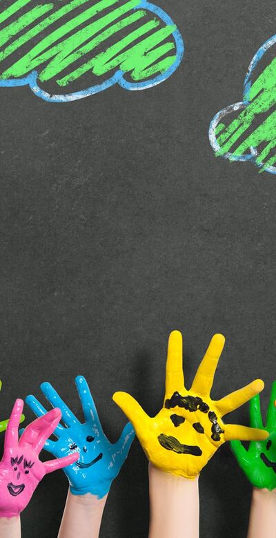 Bunte Kinderhände mit aufgemalten Gesichtern vor Tafel mit gezeichneten Wolken hochgestreckt
